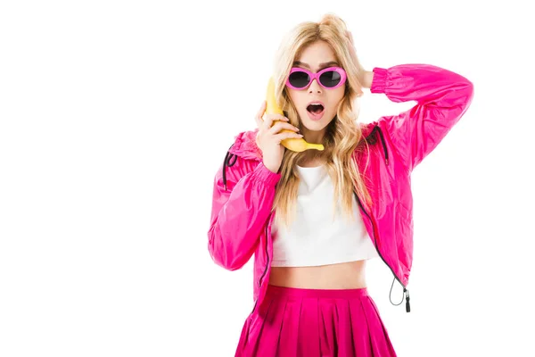 Young surprised girl wearing pink using banana like phone isolated on white — Stock Photo