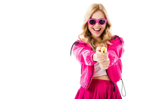 Blonde woman in pink clothes holding banana like gun isolated on white — Stock Photo