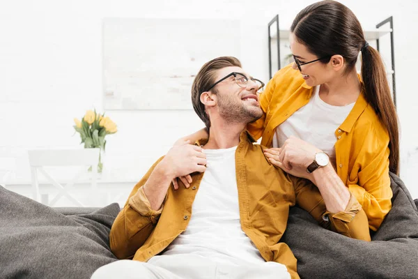 Женщина обнимает своего парня сзади, пока он сидит дома на диване — стоковое фото