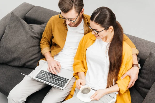 Vista de ángulo alto de la pareja joven con café y portátil sentado en el sofá juntos - foto de stock