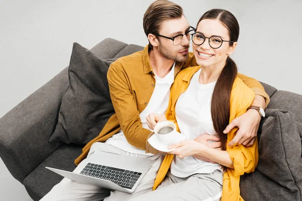 Vue grand angle de couple heureux avec café et ordinateur portable embrassant sur le canapé ensemble — Photo de stock