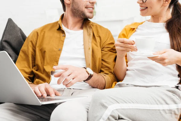 Cropped shot of couple with coffee and laptop sitting on couch together — Stock Photo