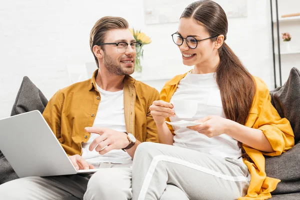 Casal feliz com café e laptop sentado no sofá juntos em casa — Fotografia de Stock