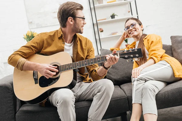 Jeune homme heureux jouant de la guitare pour petite amie heureuse — Photo de stock