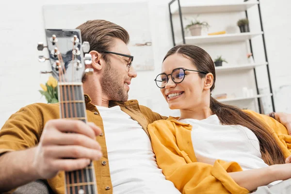 Pareja con guitarra sentado en el sofá en casa - foto de stock