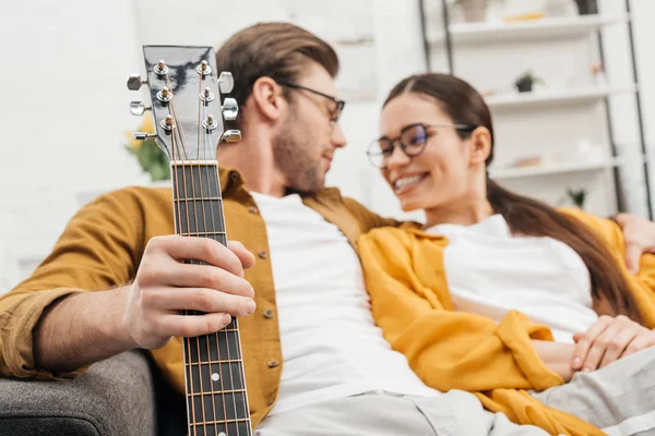 Lächelndes Paar mit Gitarre auf Sofa zu Hause — Stockfoto