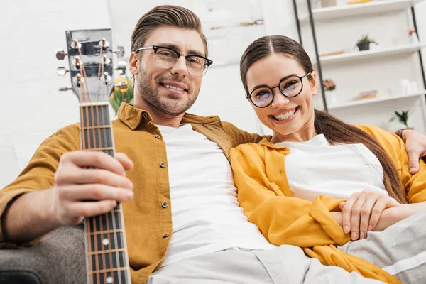 Feliz casal relaxado com guitarra sentado no sofá em casa — Fotografia de Stock