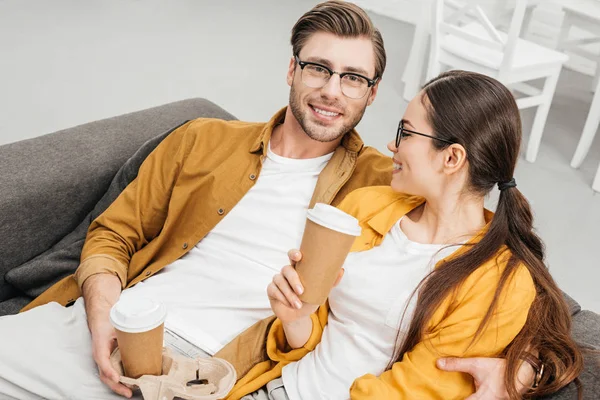 Высокий угол зрения молодой счастливой пары, пьющей кофе из бумажных стаканчиков на диване — стоковое фото
