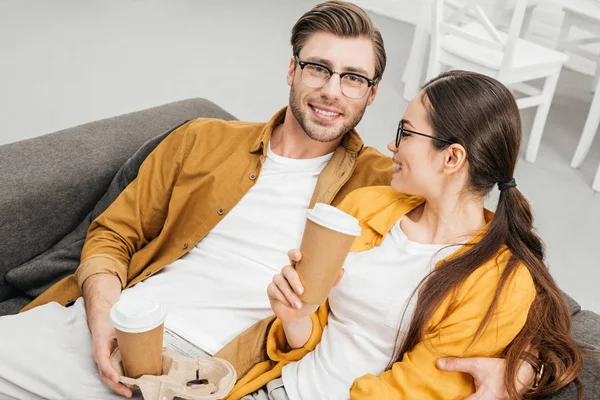 Vista de ángulo alto de la joven pareja feliz bebiendo café de tazas de papel en el sofá - foto de stock