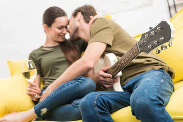 Man cuddling with smiling girlfriend while she holding glass of wine on couch at home — Stock Photo