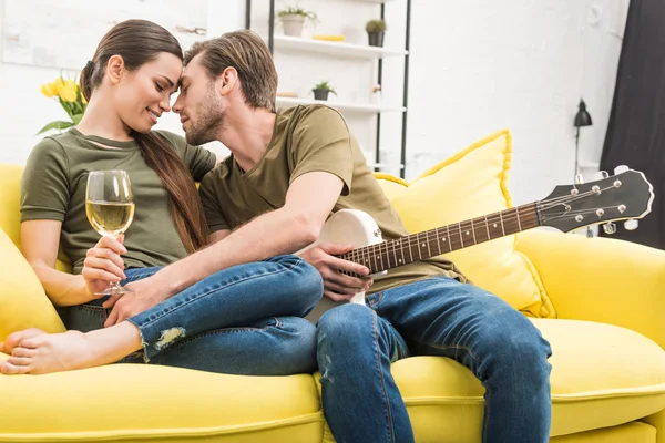 Man cuddling with girlfriend while she holding glass of wine on couch at home — Stock Photo