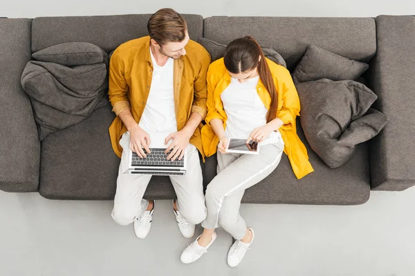 Overhead view of young couple using digital devices on cozy couch at home — Stock Photo
