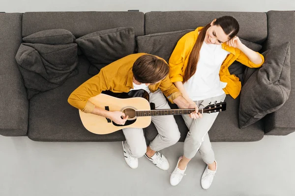 Вид зверху на людину, що грає на гітарі зі своєю дівчиною на дивані вдома — стокове фото