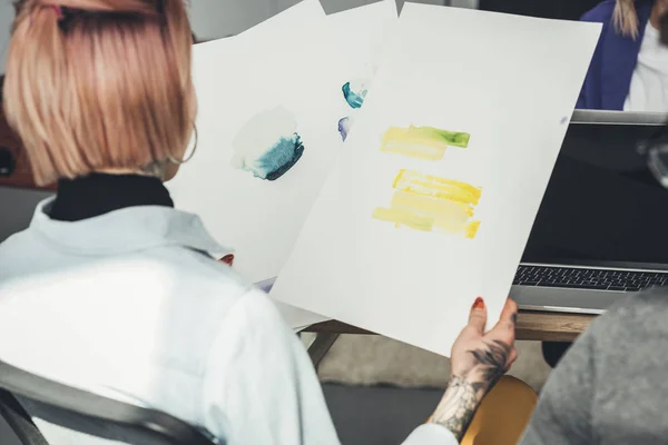 Back view of tattooed designer looking at sketches at workplace in office — Stock Photo