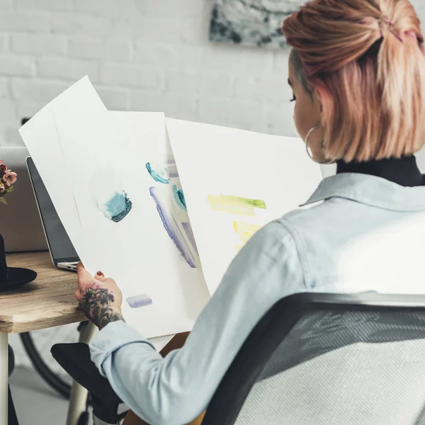 Back view of tattooed designer looking at sketches at workplace in office — Stock Photo