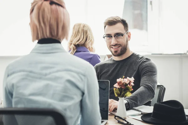 Избирательный фокус улыбающегося бизнесмена в очках на рабочем месте в офисе — стоковое фото