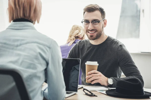 Enfoque selectivo de sonriente hombre de negocios en gafas con café para ir en el lugar de trabajo en la oficina - foto de stock