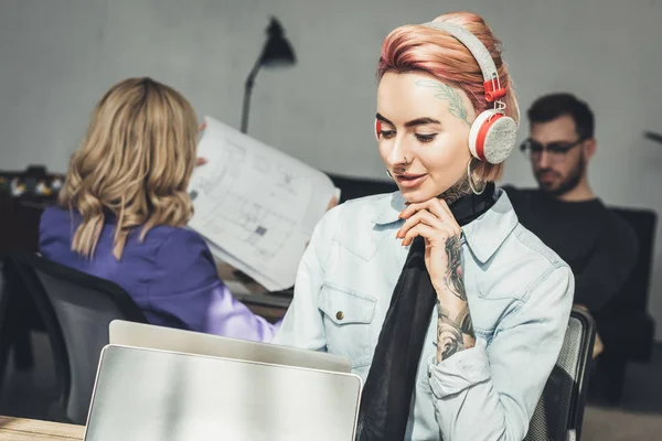 Enfoque selectivo de mujer de negocios tatuada en auriculares en el lugar de trabajo en la oficina - foto de stock