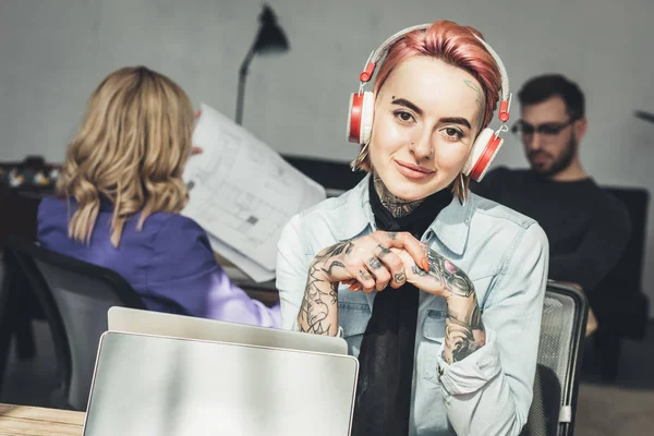 Accent sélectif de femme d'affaires tatouée dans les écouteurs sur le lieu de travail dans le bureau — Photo de stock