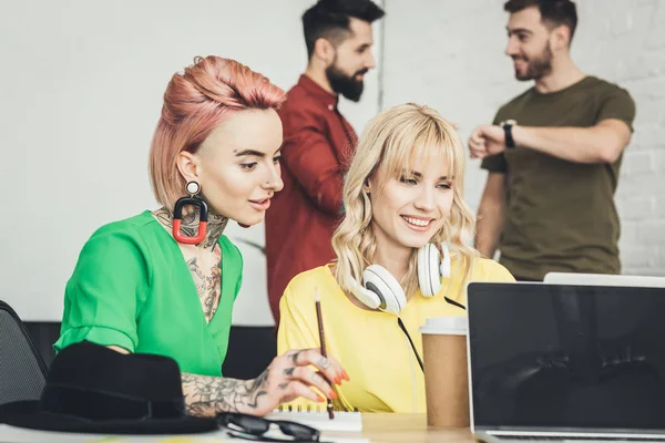 Empresarias creativas que trabajan en el proyecto juntas mientras sus colegas hablan detrás en la oficina - foto de stock