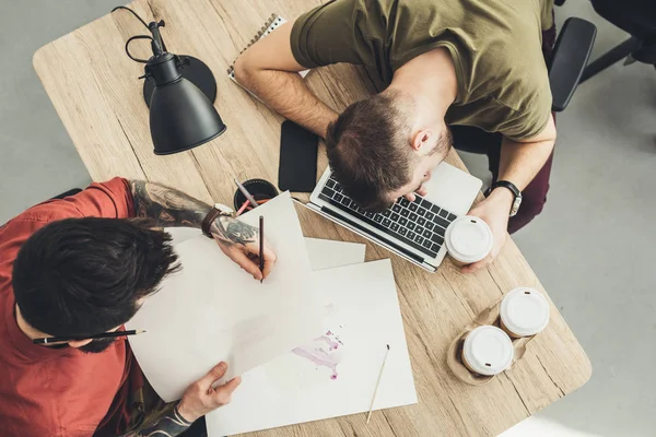 Blick von oben auf Designer und schlafenden Mitarbeiter am Tisch im Büro — Stockfoto