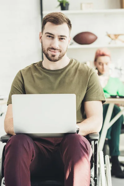 Вибірковий фокус усміхненого інваліда з ноутбуком і колегою позаду в офісі — стокове фото