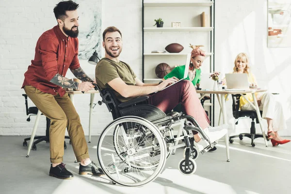 Empresário com deficiência com laptop com colega por perto e empresárias por trás no escritório — Fotografia de Stock