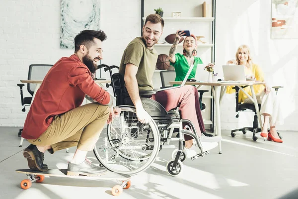 Behinderter Geschäftsmann mit Laptop mit Kollegin auf Skateboard und Geschäftsfrau im Büro — Stockfoto