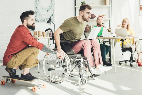 Disabled businessman with laptop with colleague on skateboard and businesswomen behind in office — Stock Photo