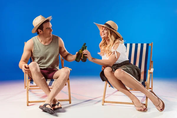 Homme et femme buvant de la bière reposant sur des chaises longues sur fond bleu — Photo de stock