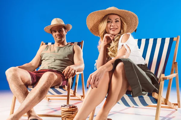 Jeune femme souriante assise sur une chaise longue par un homme et pile de crêpes sur fond bleu — Photo de stock