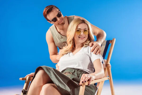 Mann umarmt Frau im Liegestuhl auf blauem Hintergrund — Stockfoto