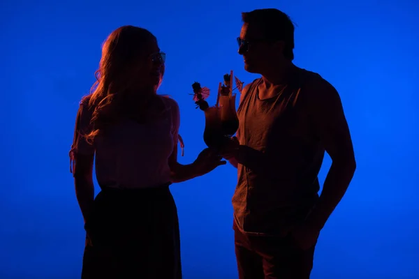 Belles silhouettes de couple pendantes avec des cocktails isolés sur bleu dans la lumière sombre — Photo de stock