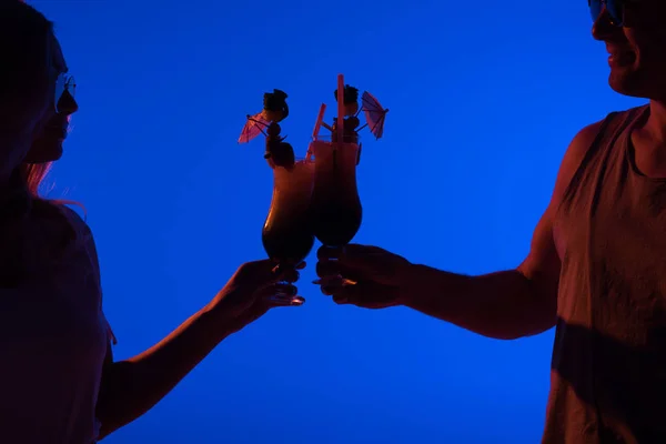Mann und Frau prosten sich mit Cocktails zu, die in dunklem Licht isoliert auf blauem Grund stehen — Stockfoto