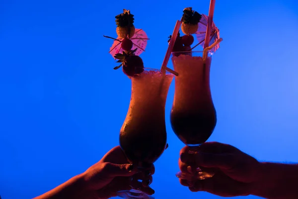 Close-up view of cocktails in male and female hands isolated on blue in dark light — Stock Photo