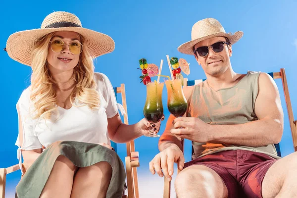 Junges attraktives Paar prostet sich mit Cocktails in Liegestühlen vor blauem Hintergrund zu — Stockfoto
