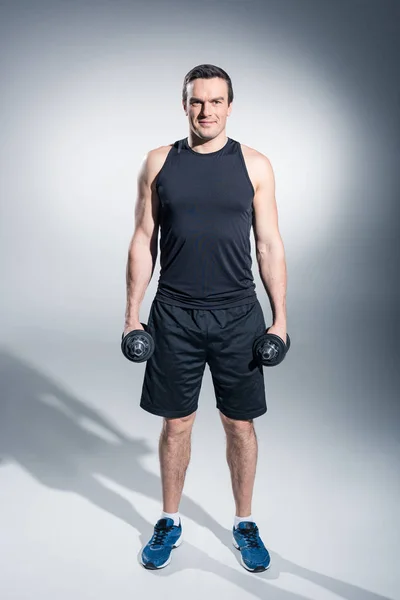 Hombre activo haciendo ejercicio con pesas sobre fondo gris — Stock Photo