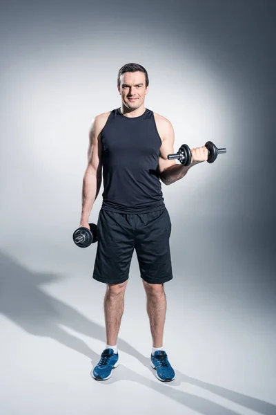 Young man athlete lifting dumbbells on grey background — Stock Photo