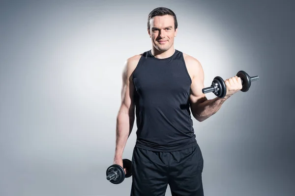 Sportsman working out with dumbbells on grey background — Stock Photo
