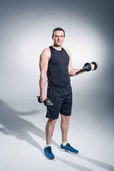 Young man athlete exercising with dumbbells on grey background — Stock Photo