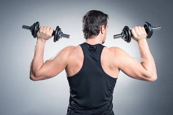 Rear view of man exercising with dumbbells on grey background — Stock Photo