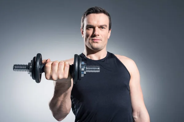 Joven atleta haciendo ejercicio con mancuerna sobre fondo gris - foto de stock