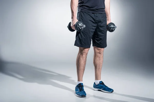 Close-up view of sportsman working out with heavy dumbbells on grey background — Stock Photo