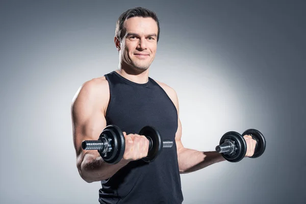 Lächelnder Mann beim Hantelheben auf grauem Hintergrund — Stockfoto