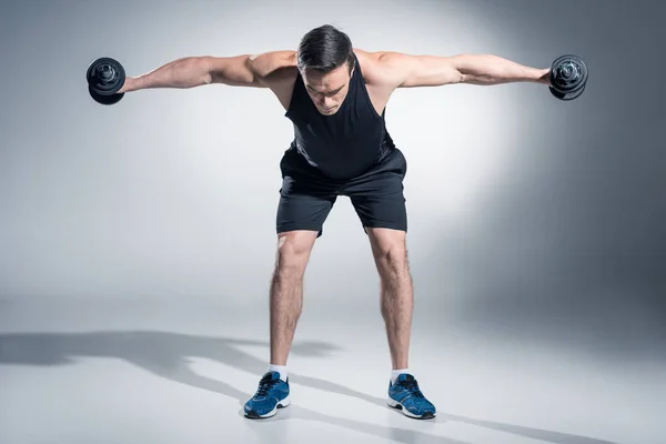 Atractivo atleta hombre levantando pesas sobre fondo gris - foto de stock