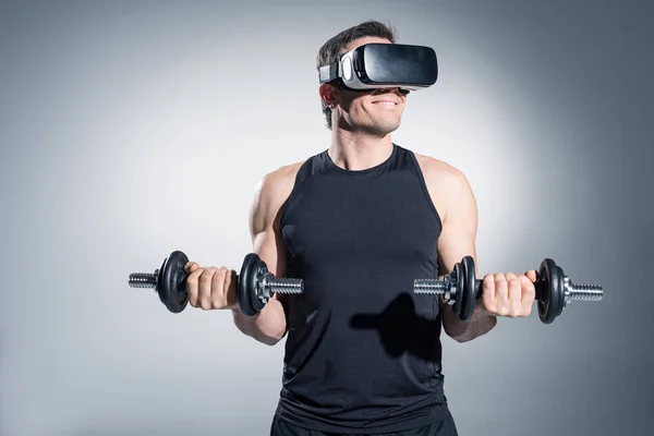Active man training with dumbbells while wearing vr glasses on grey background — Stock Photo