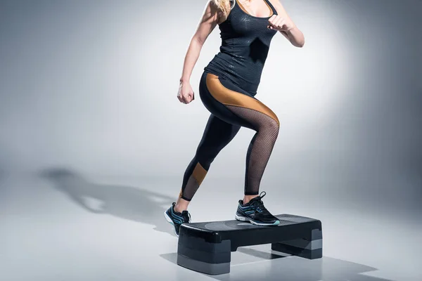 Young woman exercising on step platform on grey background — Stock Photo