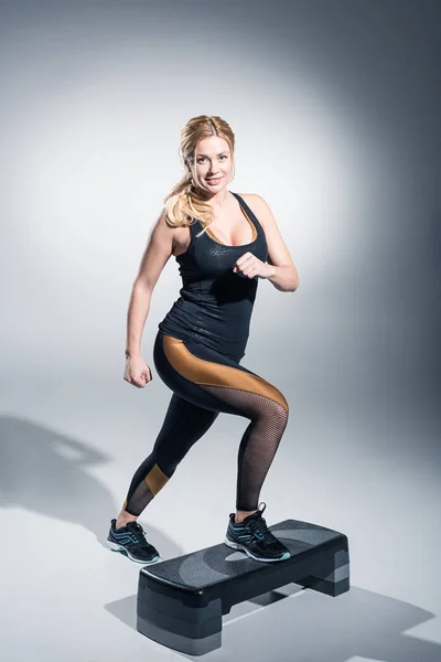 Blondine trainiert auf Trittplattform auf grauem Hintergrund — Stockfoto