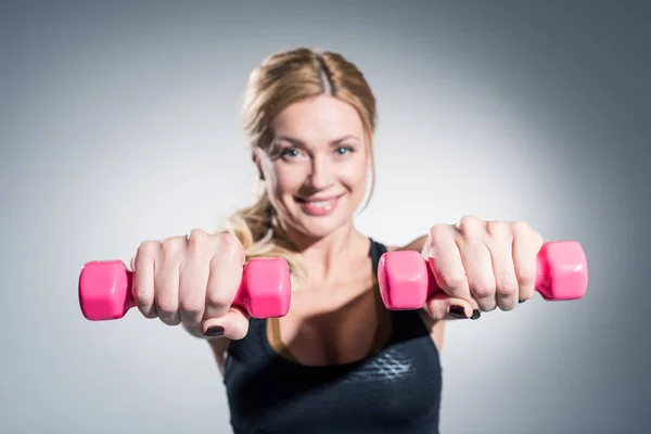 Mujer joven haciendo ejercicio con pesas sobre fondo gris - foto de stock