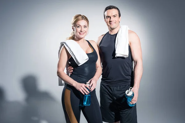 Hombre y mujer atléticos con toallas sosteniendo botellas deportivas sobre fondo gris - foto de stock
